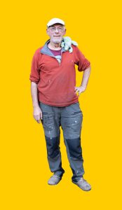 02 Gelber Hintergrund, davor ein Mensch in Arbeitskleidung im Portrait