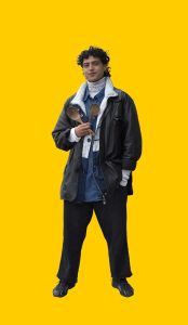 03 Gelber Hintergrund, davor ein Mensch im Portrait, der einen Kochlöffel in der Hand hält