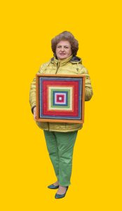 09 Gelber Hintergrund, davor ein Mensch im Portrait, der ein Bild in der Hand hält