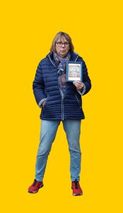 15 Gelber Hintergrund, davor ein Mensch im Portrait, der ein kleines Bild in der Hand hält